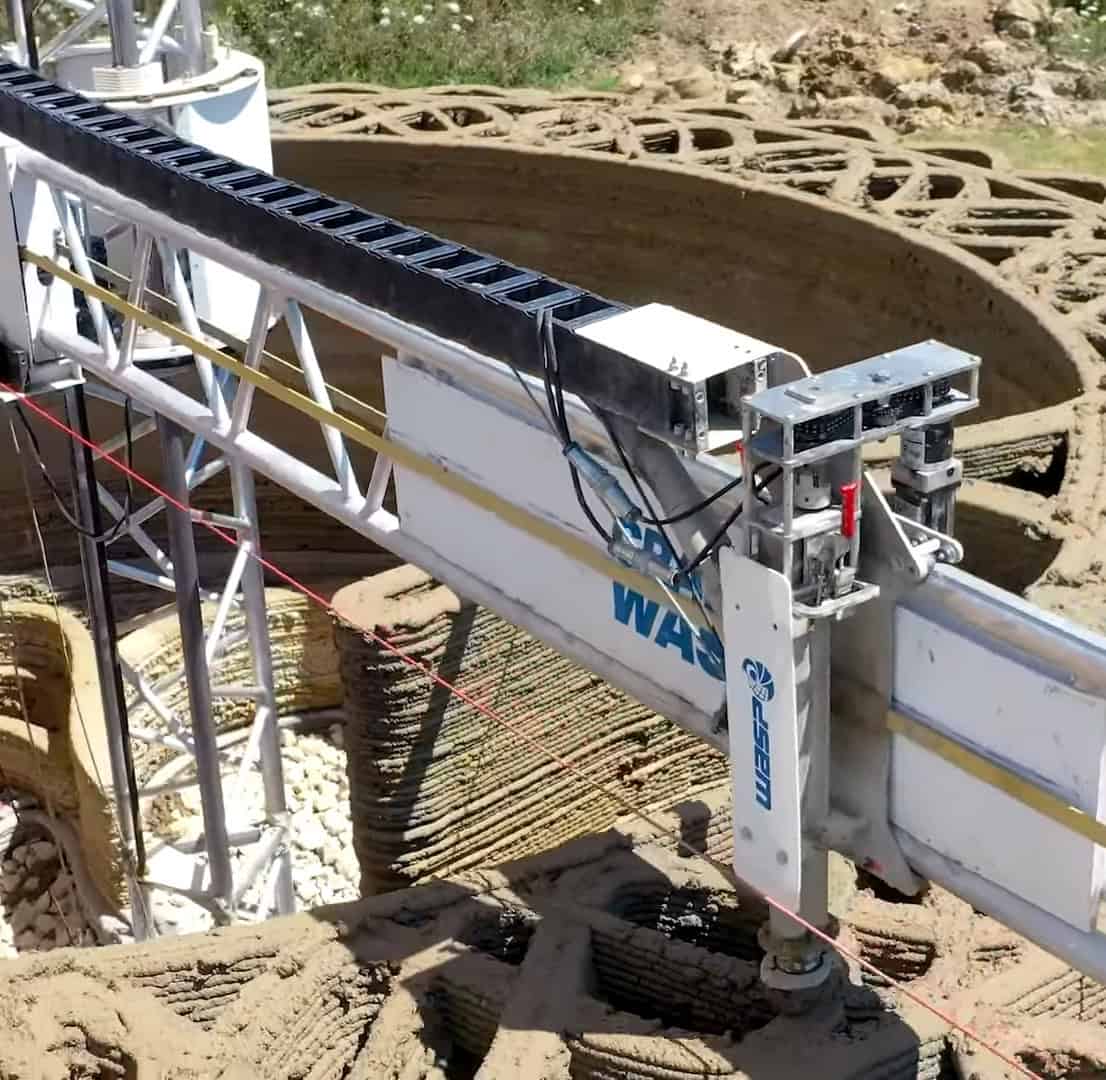 A gantry 3D printer arm extruding a layered wall during house construction