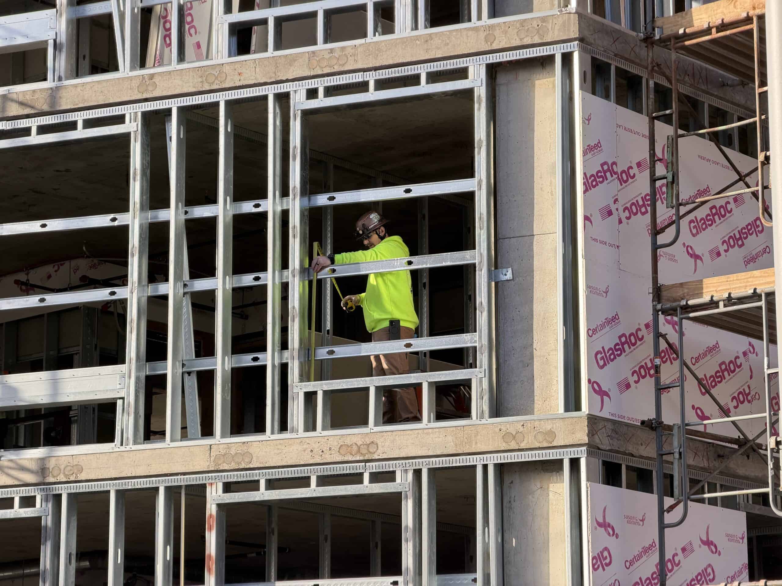 Construction worker in high-visibility vest measuring framing on a Portland, Oregon job site