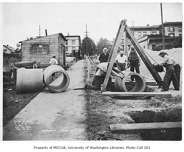Underground sewer-line construction crew installing pipe in an open trench
