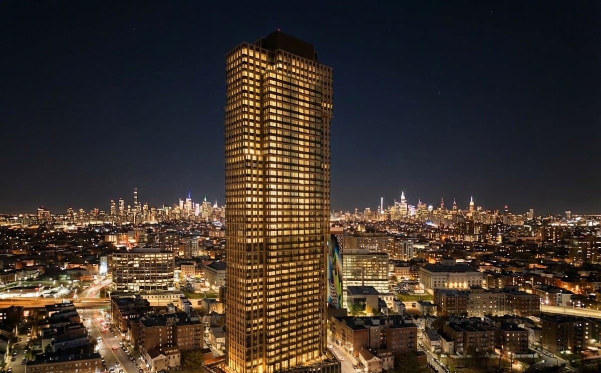 The completed 505 Summit residential tower lit at night over Journal Square in Jersey City