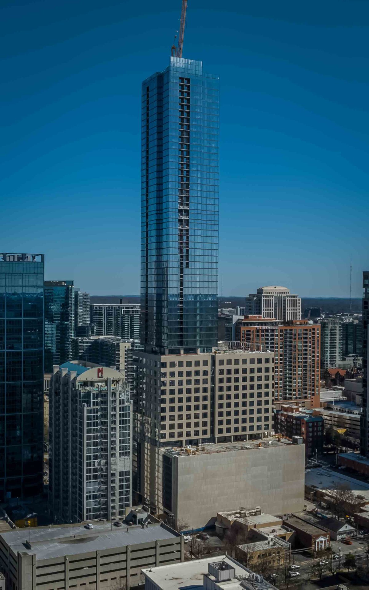 The Alina tower at 1072 West Peachtree Street rising above Midtown Atlanta, its glass curtain wall complete to the top with a tower crane still standing on the roof.