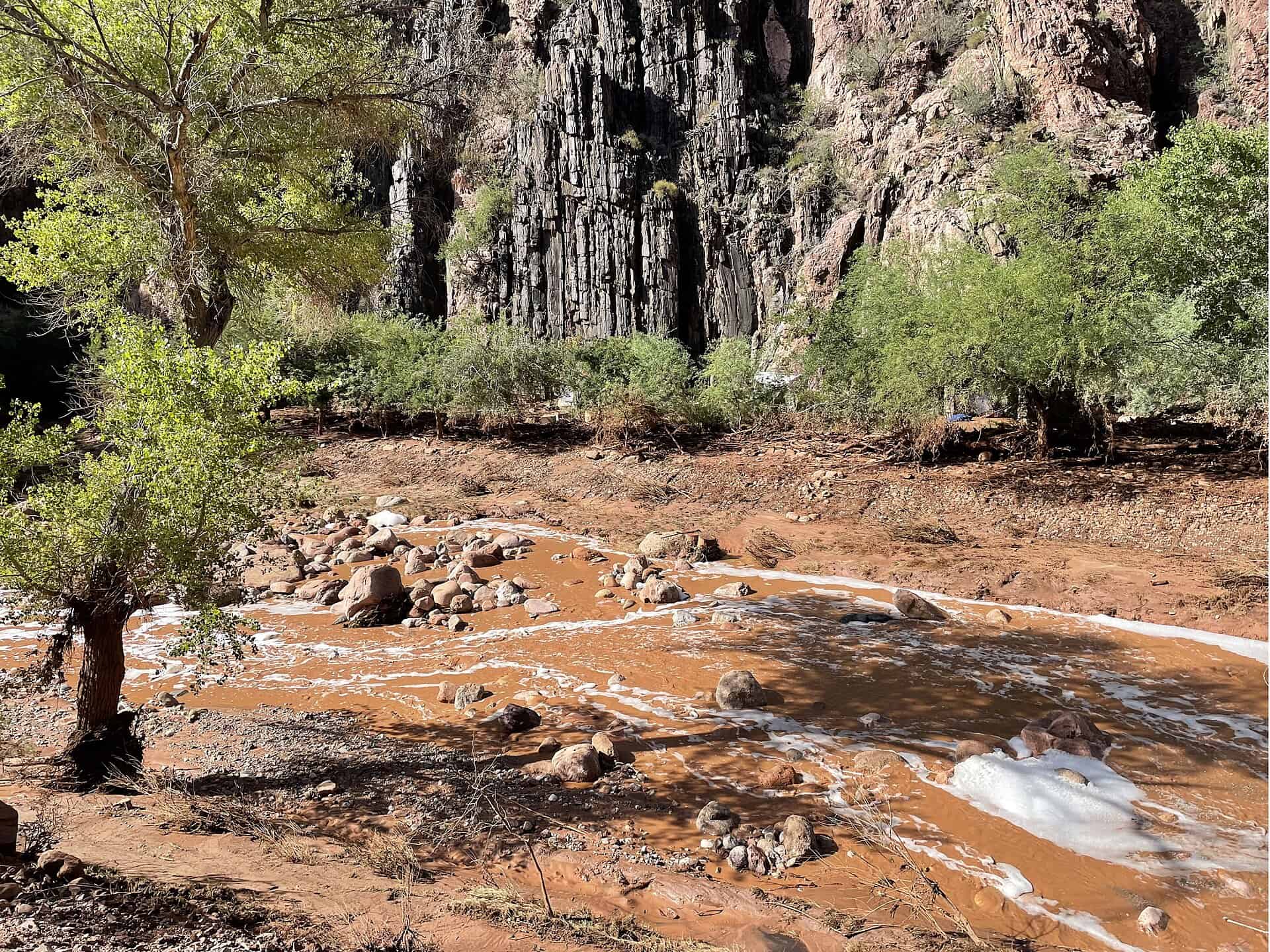 Bright Angel Creek runs muddy through a scoured, debris-filled bed after the August 2026 flash flood