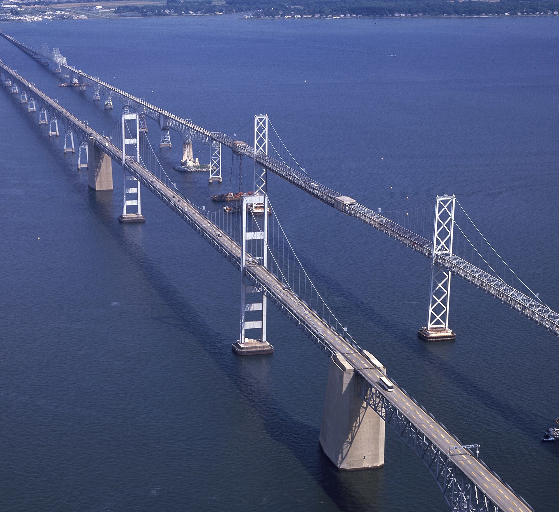 Aerial view of the twin Chesapeake Bay Bridge spans over the bay, with the 1952 eastbound span and its X-braced suspension towers on the right