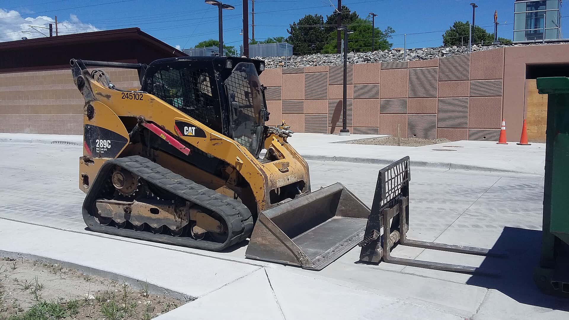 A yellow compact track loader sits on new concrete paving at a transit station construction site