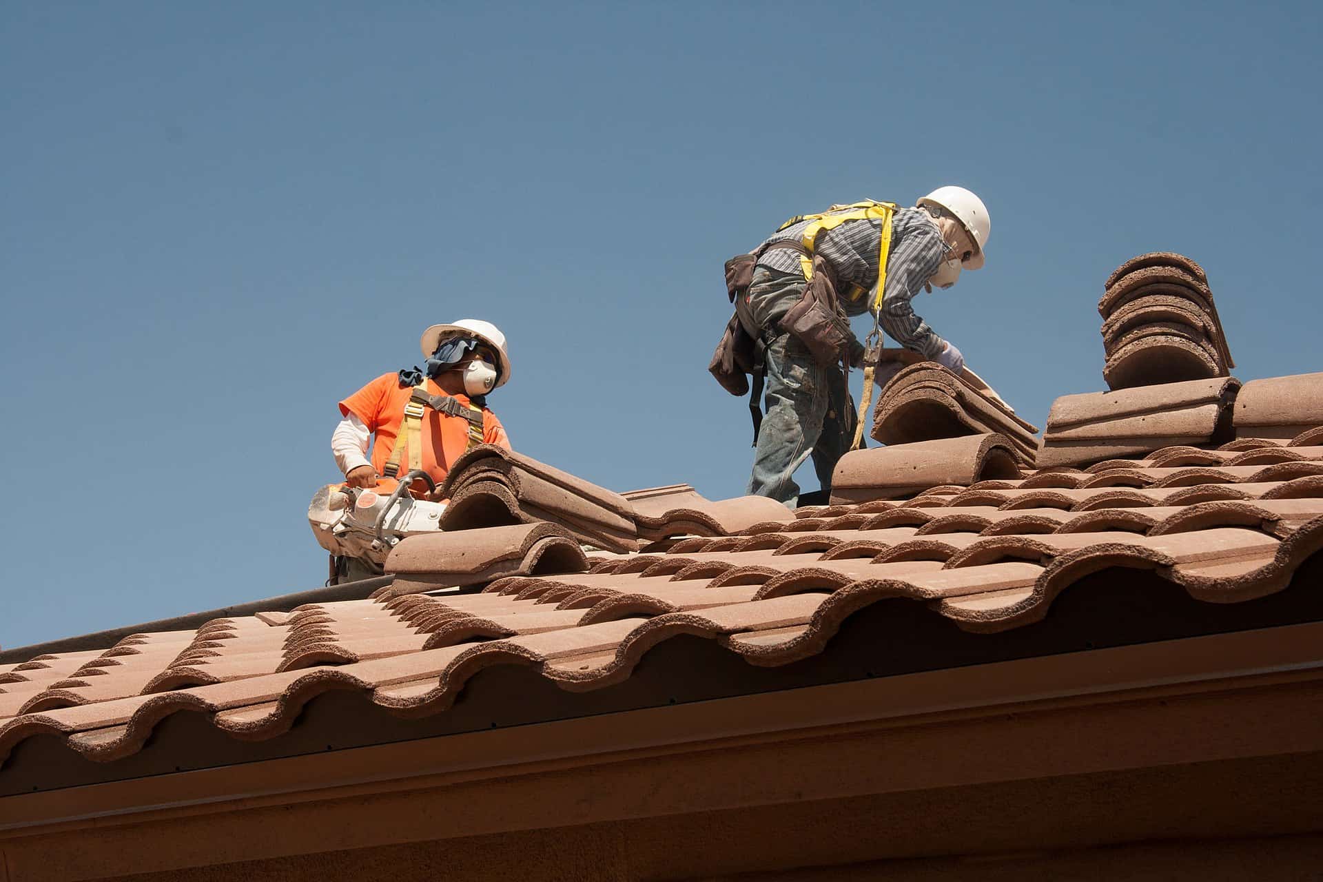 Your Crew Is Trained on Your Hazards. The Trade Working Above Them Isn't. Roofing workers tied off to a fall prevention system on a sloped roof