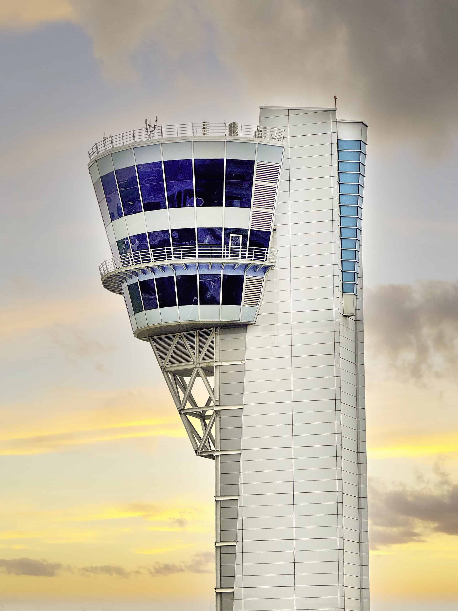 An FAA air traffic control tower with a glazed cab rises against a sunset sky