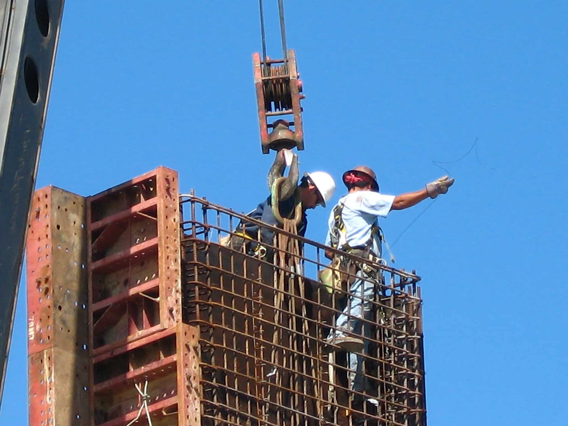 Two hard-hatted workers set formwork atop a rebar column cage on a Houston construction project