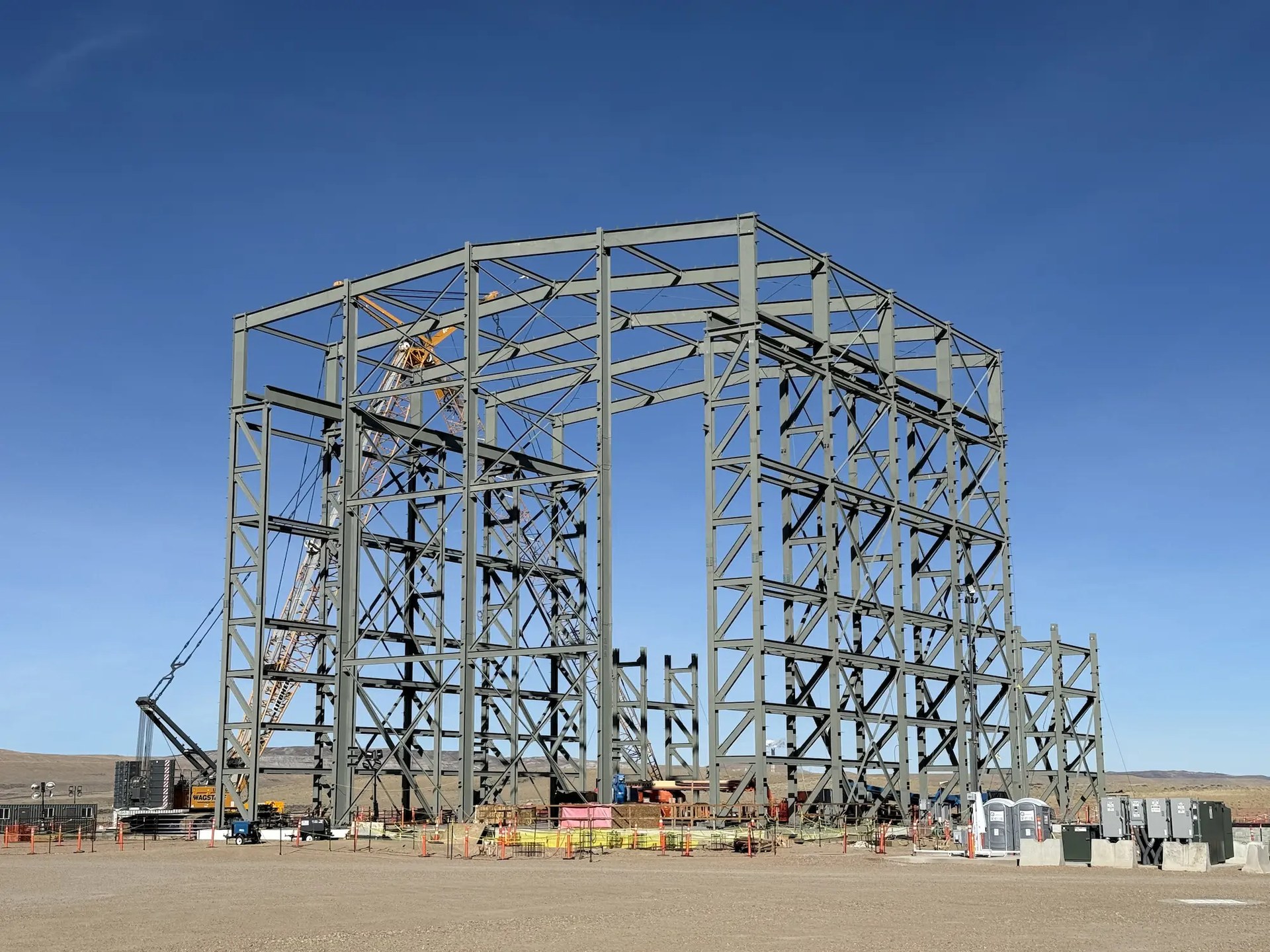 The structural steel frame of the energy island building at TerraPower's Natrium Kemmerer Unit 1 site in Wyoming, with a crawler crane working behind it on the open high-desert pad.