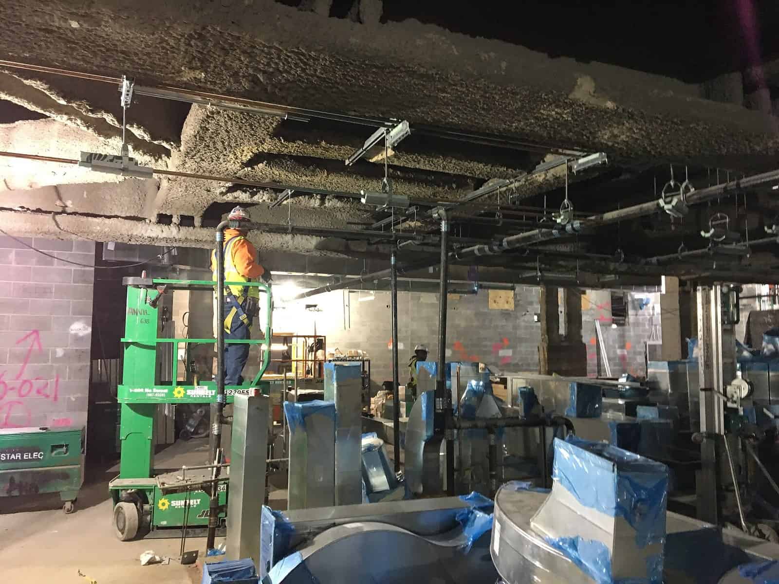 Worker on a vertical lift installing overhead ductwork with sheet metal sections staged below