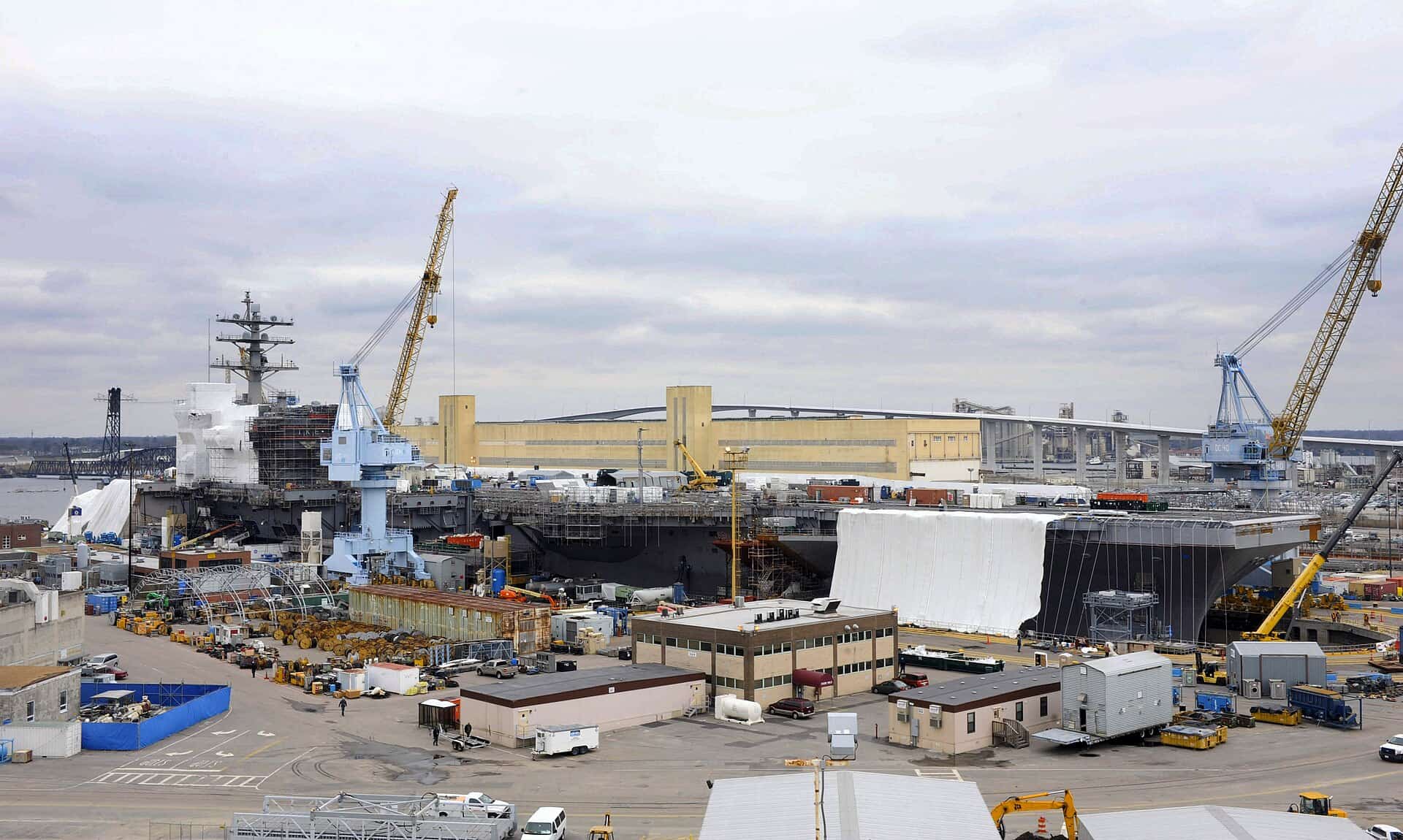 An aircraft carrier sitting dewatered in a graving dock at Norfolk Naval Shipyard with portal cranes rigged over the hull