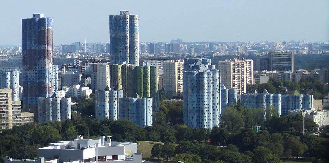 The cylindrical Tours Aillaud cloud towers in Nanterre with their blue mosaic facades, La Défense towers and the Eiffel Tower in the distance