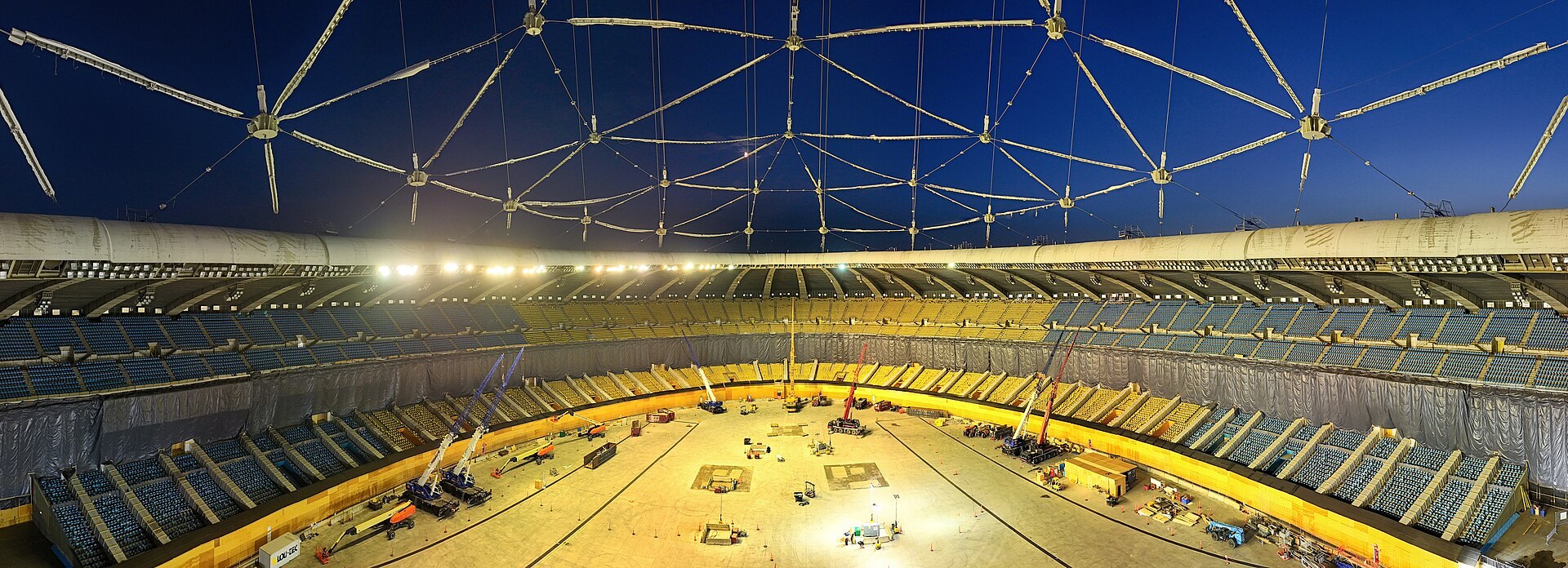 Inside Montreal Olympic Stadium in October 2024 with the old roof membrane removed, its cable network open to the night sky and cranes working on the stadium floor