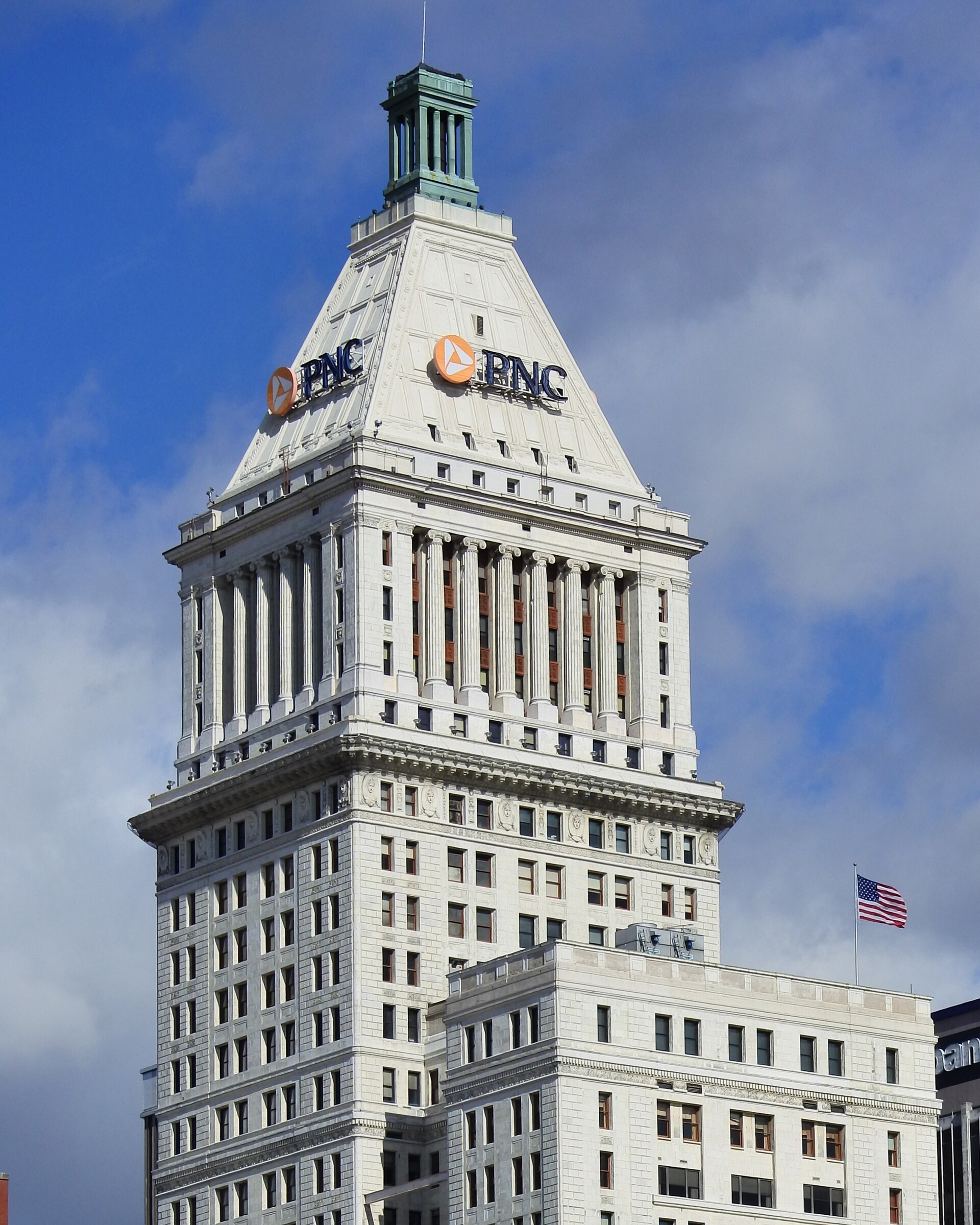 Upper two-thirds of the tower and its pyramid crown in 2015, still carrying PNC signs, with the lower annex in front