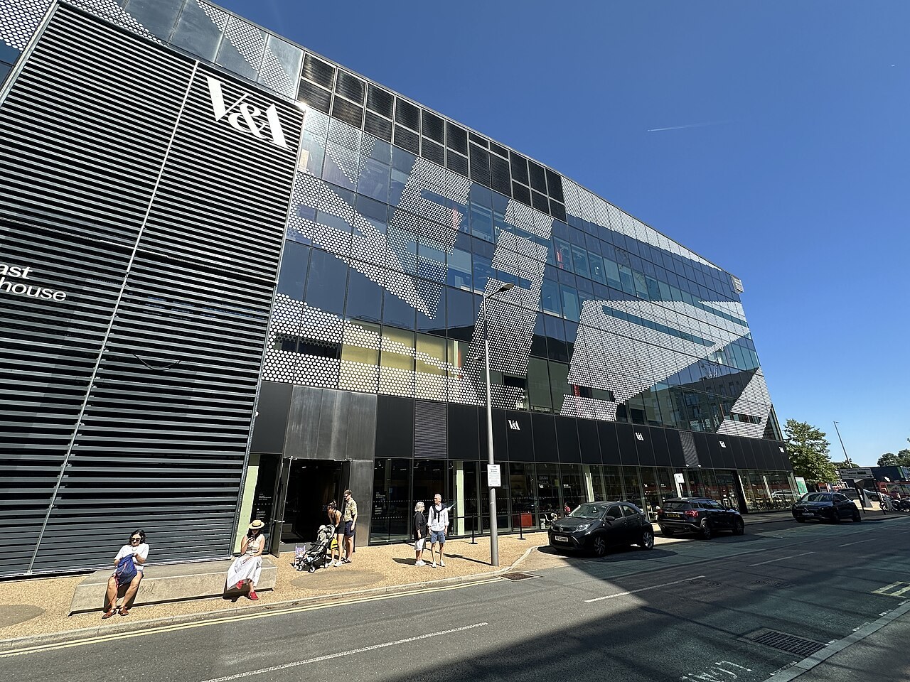 Street facade of the V&A East Storehouse at Here East, with V&A lettering on black louvres and a perforated metal screen over the glazing